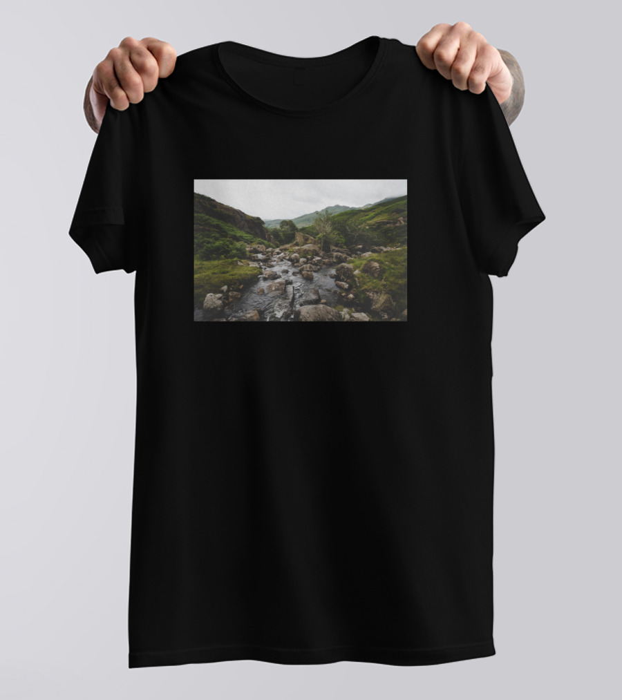 Lush Green Grass Surrounding Rocky River Amidst Nature's Tranquil Landscape T-Shirt